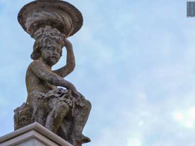 Pi� in alto una cornice a dentelli, che corre lungo tutto l�edificio, cinge un terrazzino abbellito da due statue di bambini che reggono un vaso sul capo